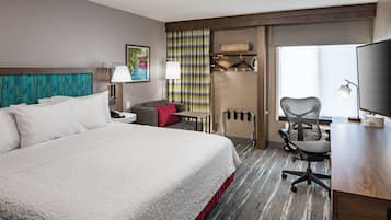 A hotel room with a large bed, a desk, a chair, a TV, and a window with curtains.