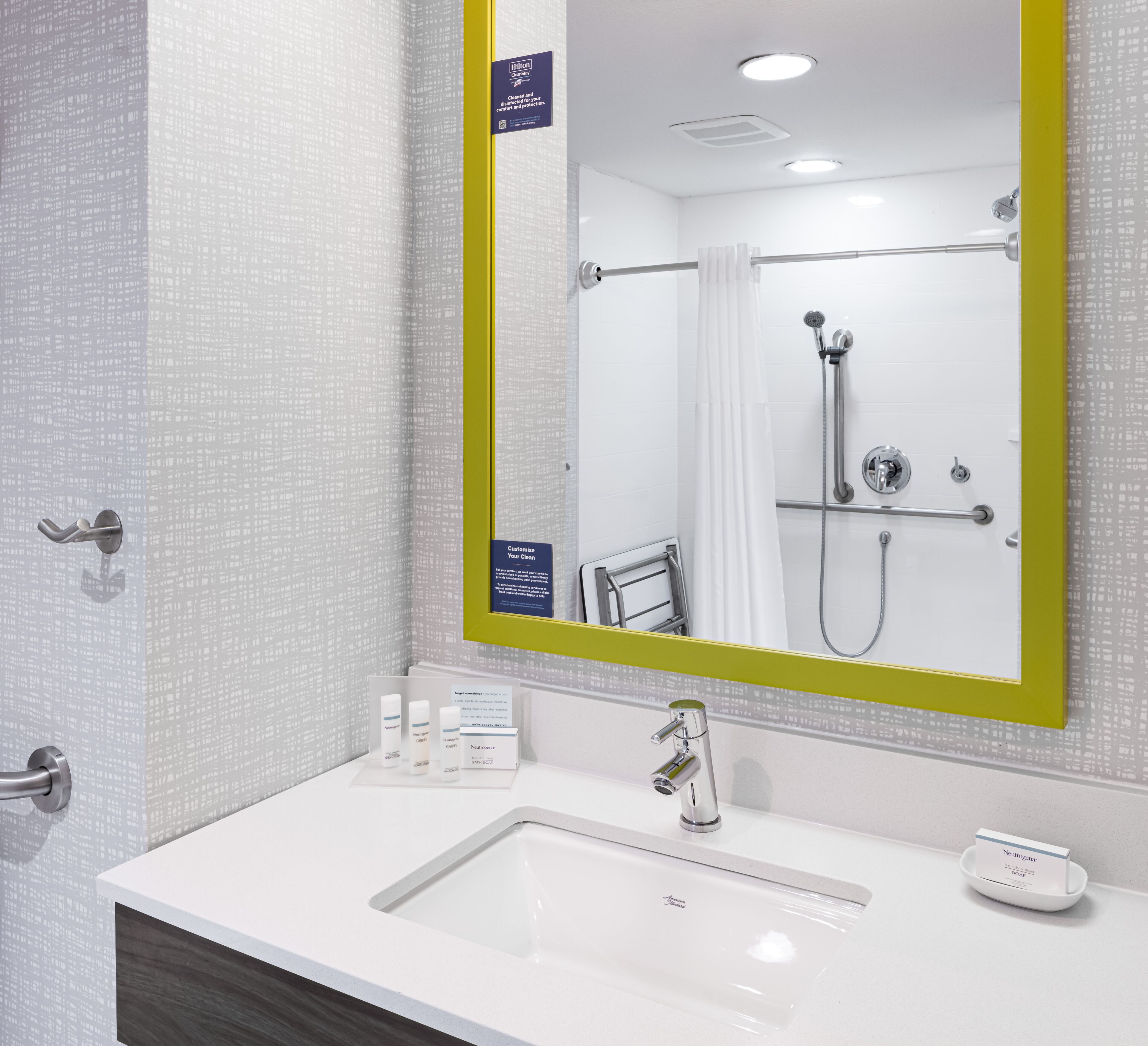 Casa de banho moderna com lavatório branco, espelho com moldura amarela e zona de duche com chuveiro manual.