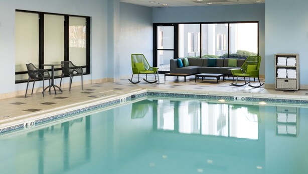 Un área de piscina con un conjunto de asientos, que incluye sillas y un sofá, y suelo de baldosas.