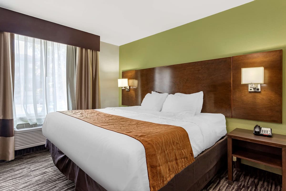 Une chambre d’hôtel avec un grand lit, deux lampes de chevet, un téléphone et une fenêtre avec des rideaux.