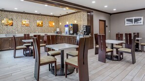 Un restaurant avec plusieurs tables et chaises, un comptoir avec une machine à café et des œuvres d’art murales.