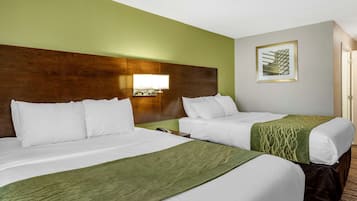 A hotel room with two beds, a wooden headboard, a green wall, and a framed picture.