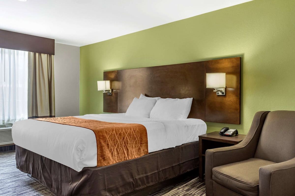 Une chambre d’hôtel avec un lit, une chaise, une table de chevet avec un téléphone et une lampe fixée au mur.