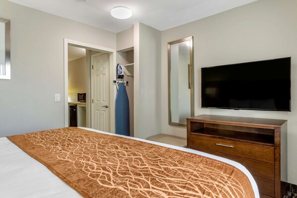 A hotel room with a large bed, a flat-screen TV, a wooden dresser, and a mirror on the wall.