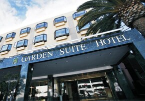 L'esterno del Garden Suite Hotel, con facciata moderna, ampie finestre e una palma sullo sfondo.