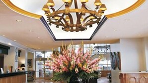 En lobby med en stor lysekrone, en receptionsdisk og en blomsteropsætning på et rundt bord.