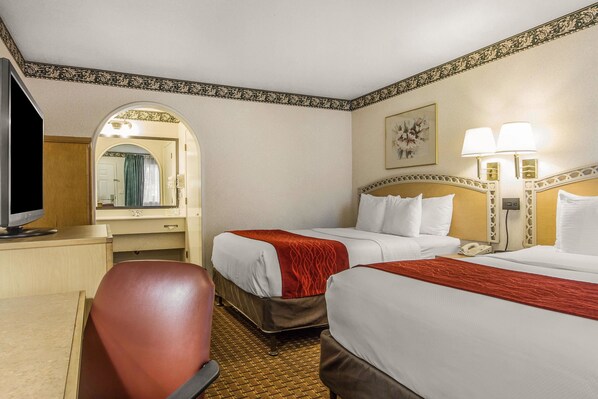 A hotel room with two beds, a desk, a chair, a television, and a mirror.