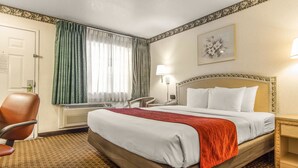 Hotellihuone, jossa on suuri sänky, tuoli, työpöytä ja ikkuna, jossa on verhot.