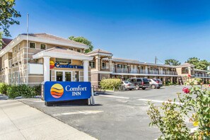 Een Comfort Inn hotel met een opvallend bord, een parkeerplaats en een rij gebouwen op de achtergrond.