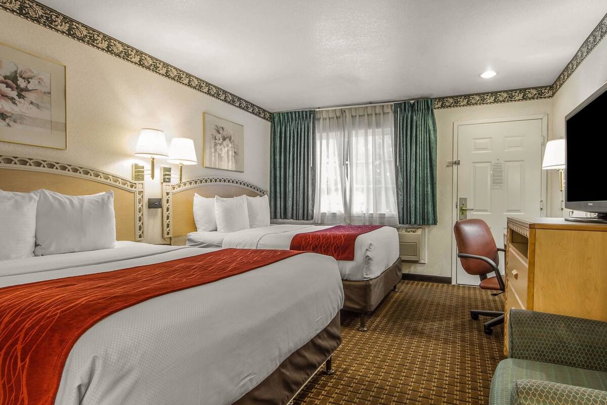 Une chambre d’hôtel avec deux lits, un bureau, une chaise, une télévision et une fenêtre avec des rideaux.