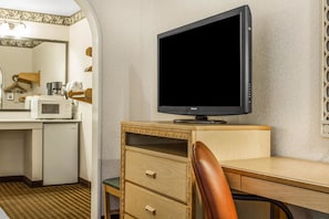 Una habitación de hotel compacta con un escritorio de madera, un televisor de pantalla plana, un microondas y un refrigerador.