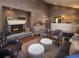 Una sala de estar acogedora con chimenea, sofá de cuero, otomanas y un comedor con una cocina al fondo.