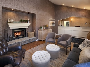 A cozy living room with a fireplace, leather sofa, ottomans, and a dining area with a kitchen in the background. - Cottage Inn By The Sea (Pismo Beach)