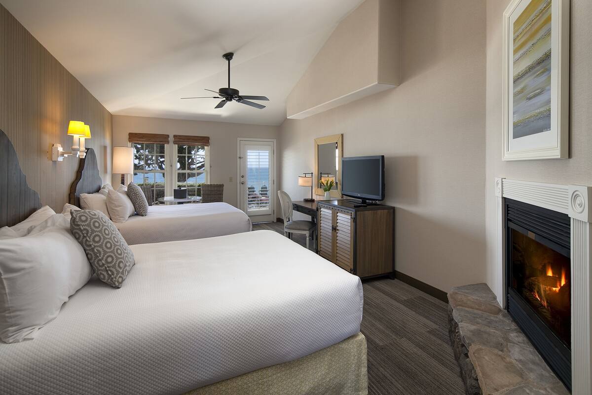 A hotel room with two beds, a television, a fireplace, and a desk.