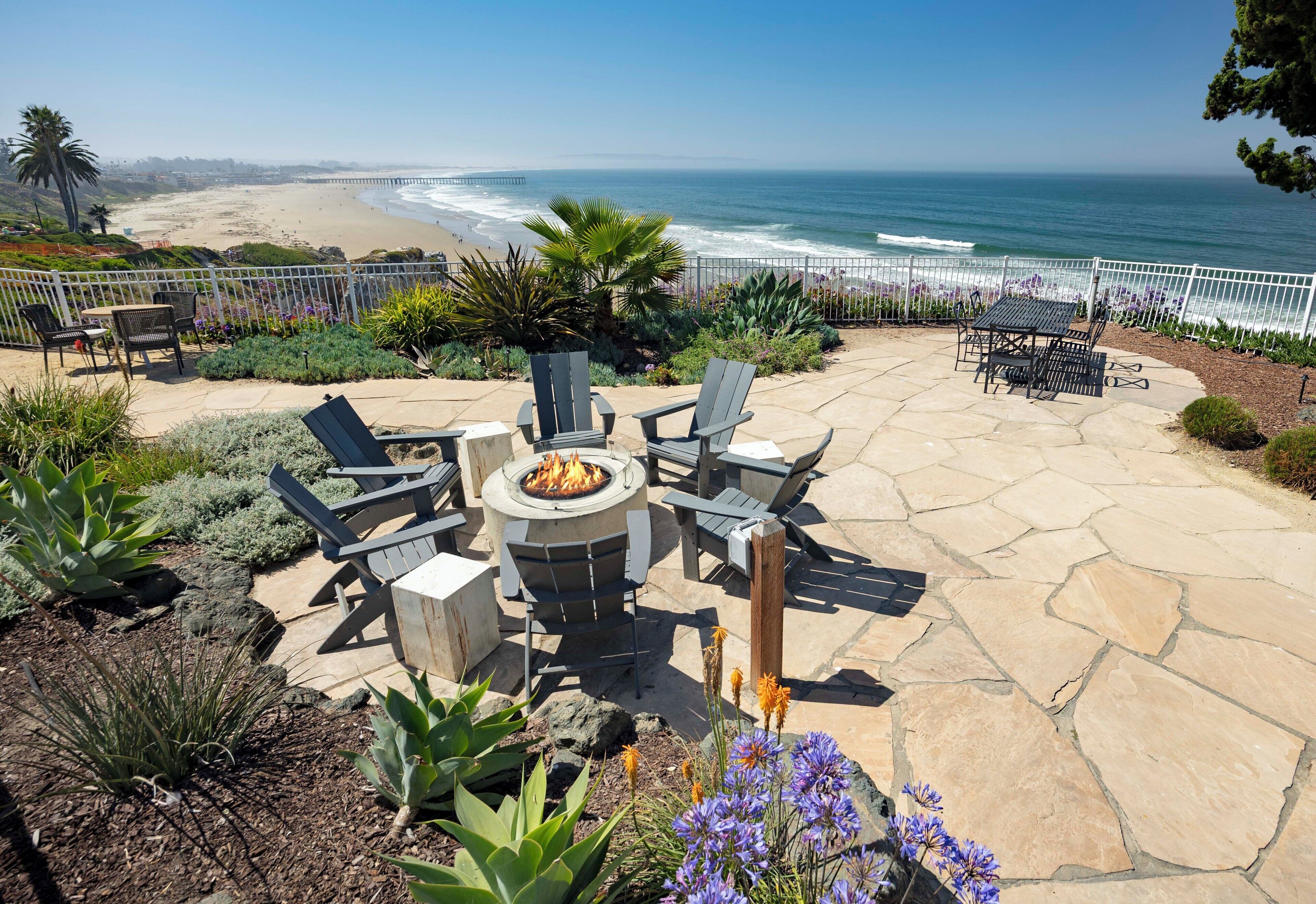 A patio with a fire pit, outdoor furniture, and a view of the beach and ocean.