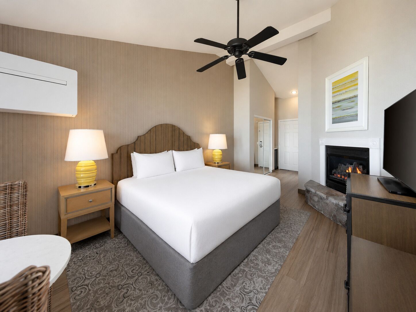 Ein Hotelzimmer mit einem Bett, zwei Nachttischlampen, einem Deckenventilator, einem Kamin, einem Fernseher und einem gerahmten Bild an der Wand.