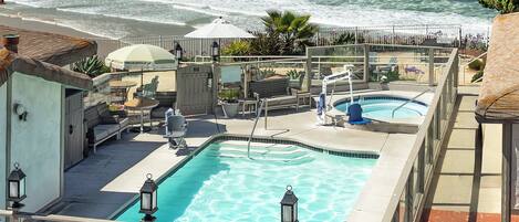 A pool area with a view of the ocean, lounge chairs, and a small deck.