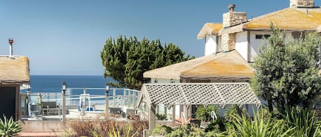 A coastal property with a terrace overlooking the sea, stone walls, and a variety of vegetation.