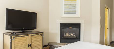 Un dormitorio con una televisión sobre un mueble de madera, una chimenea y un cuadro enmarcado en la pared.