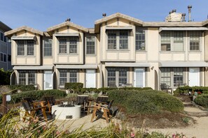 A multi-story building with a symmetrical facade, large windows, and a landscaped outdoor area with seating and a fire pit. - Cottage Inn By The Sea (Pismo Beach)