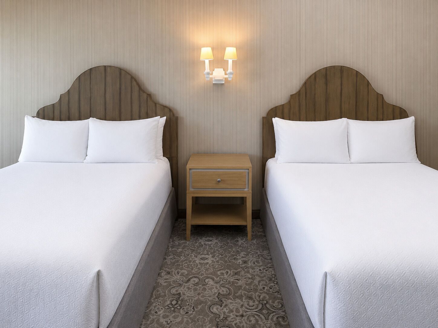 A hotel room with two beds, a nightstand with a lamp, and a patterned carpet.