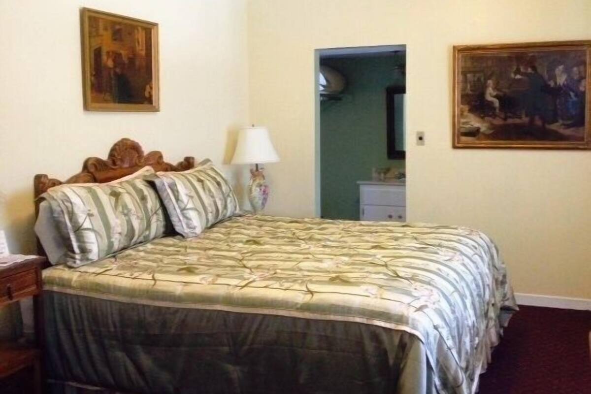 A bedroom with a bed, a nightstand, a lamp, and two paintings on the walls.