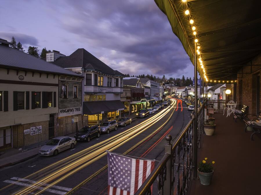 A street view at dusk with illuminated buildings and a long exposure of moving vehicles.