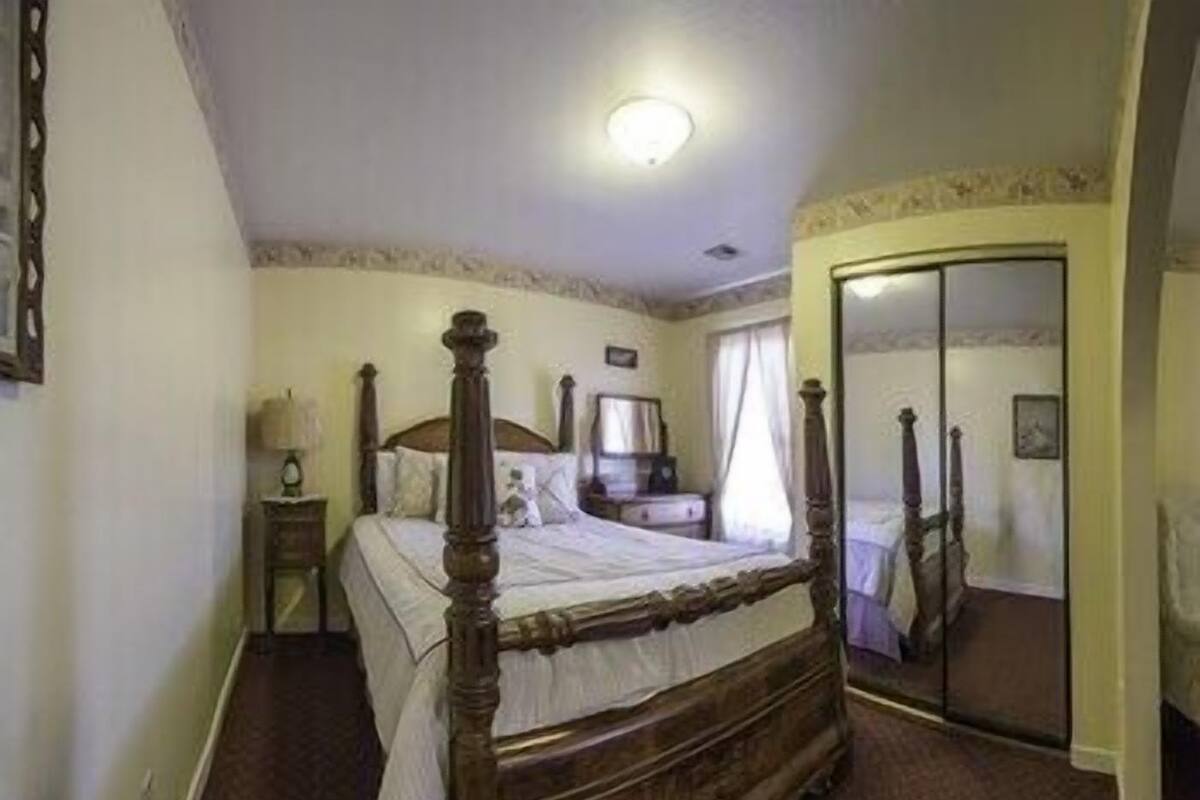A bedroom with a four-poster bed, a nightstand, a dresser, and a mirror.