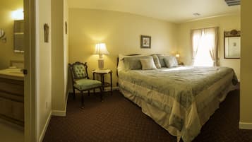 Habitación de hotel con una cama grande, una silla, una mesita de noche con lámpara y un baño visible a través de una puerta abierta.
