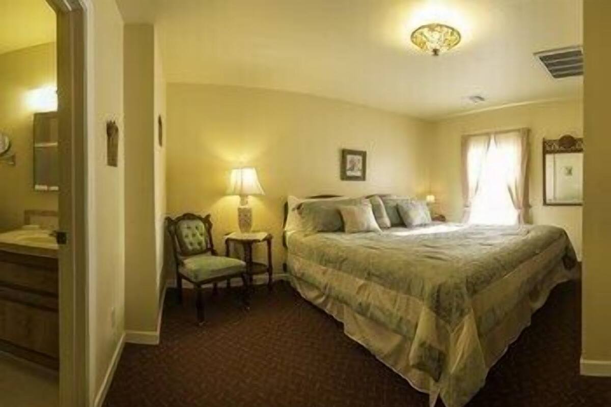 A hotel room with a bed, a chair, a lamp, and a small table.