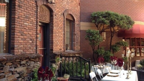An outdoor dining area with brick walls, string lights, and tables set for a meal. - Historic Cary House Hotel (Placerville)