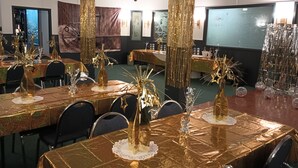 A banquet hall with tables covered in golden tablecloths, decorated with golden centerpieces and hanging decorations. - Historic Cary House Hotel (Placerville)
