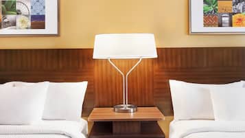 A hotel room with two beds, a nightstand with a lamp, and two framed pictures on the wall.
