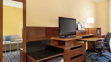 A hotel room with a wooden desk, a television, a small table, a sofa, and a lamp.
