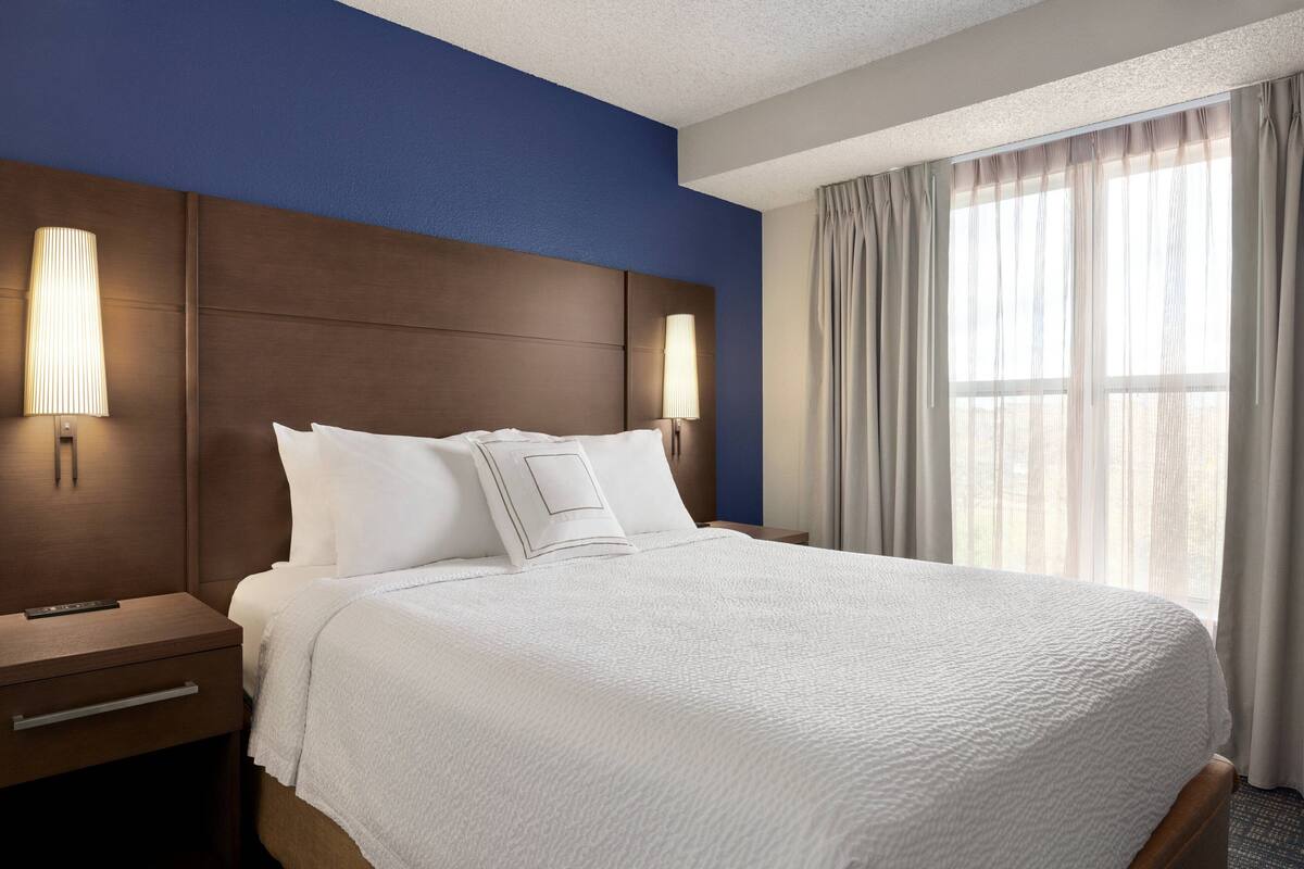 Habitación de hotel con una cama grande, dos mesitas de noche, un cabecero y una ventana con cortinas.