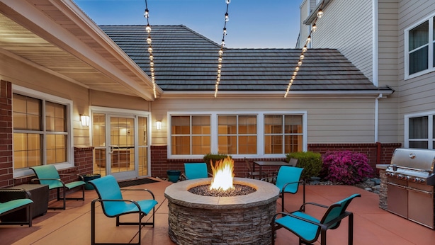 An outdoor patio with a stone fire pit, seating, and a grill.