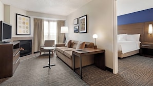 A hotel room with a sofa, a TV, a desk, a lamp, a bed, and a fireplace.