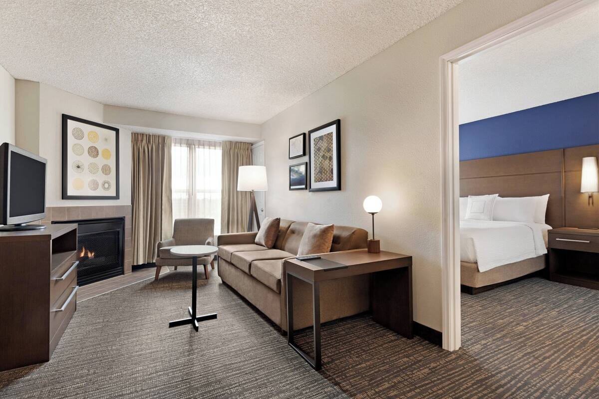 Habitación de hotel con sofá, televisión, escritorio, lámpara, cama y chimenea.