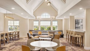 A spacious room with a high ceiling, large windows, a seating area with sofas and chairs, and a bar area with stools.