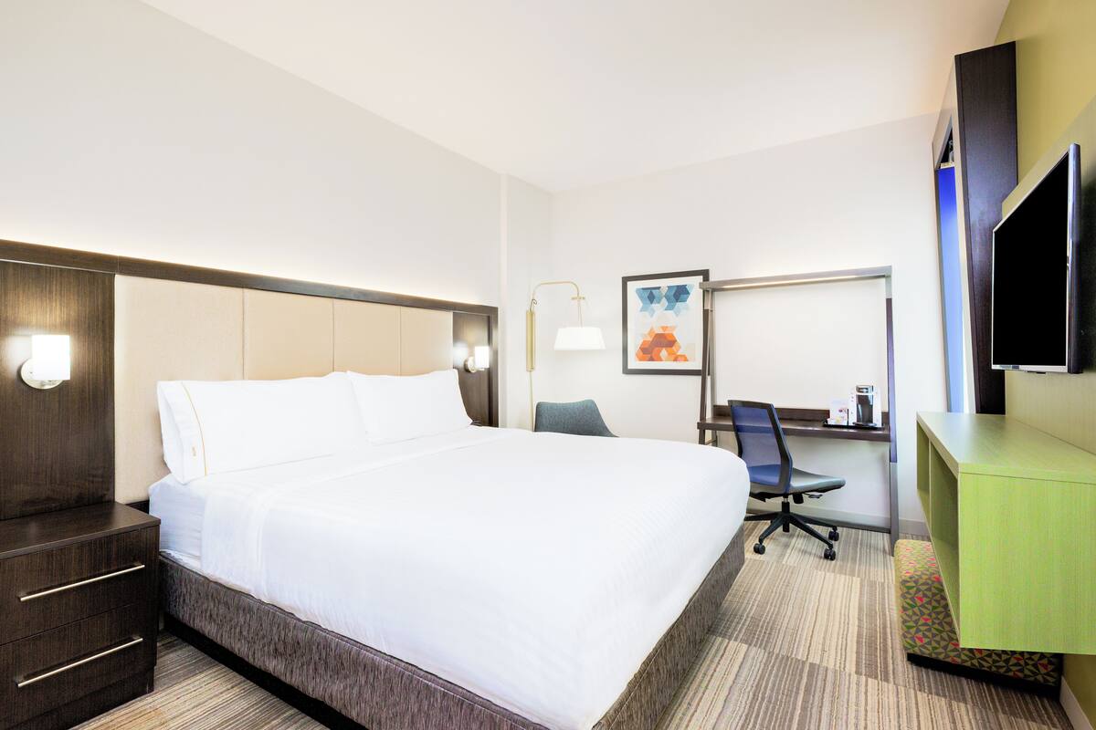 A hotel room with a large bed, a desk, a chair, and a TV.
