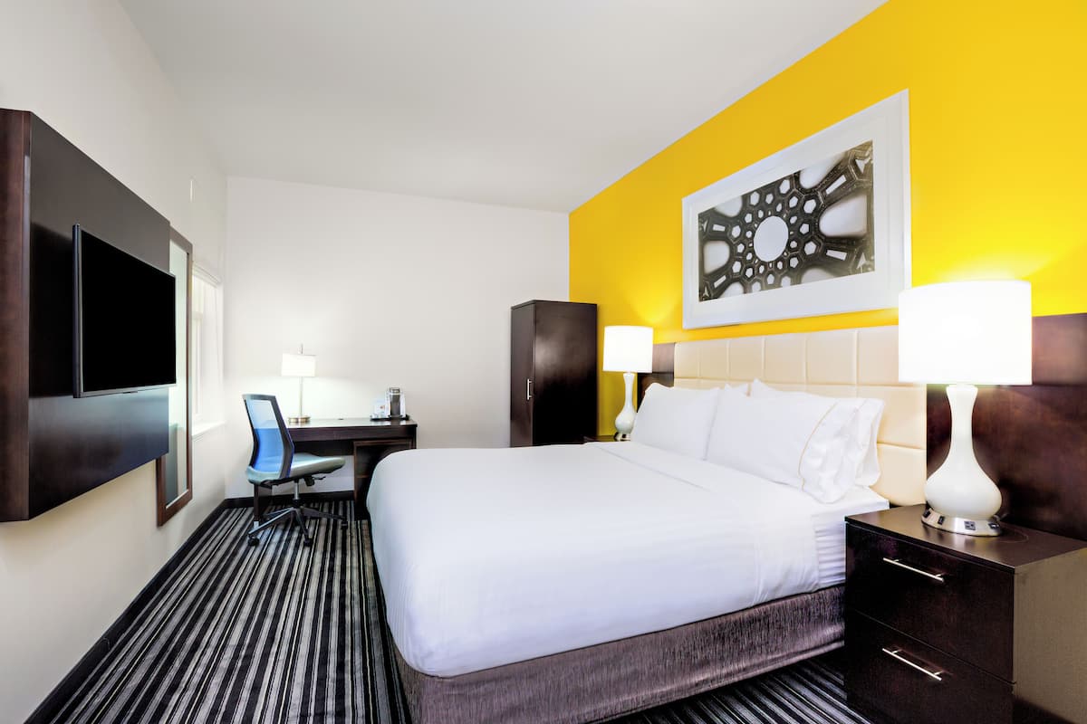 A hotel room with a large bed, a desk, a chair, and a TV.