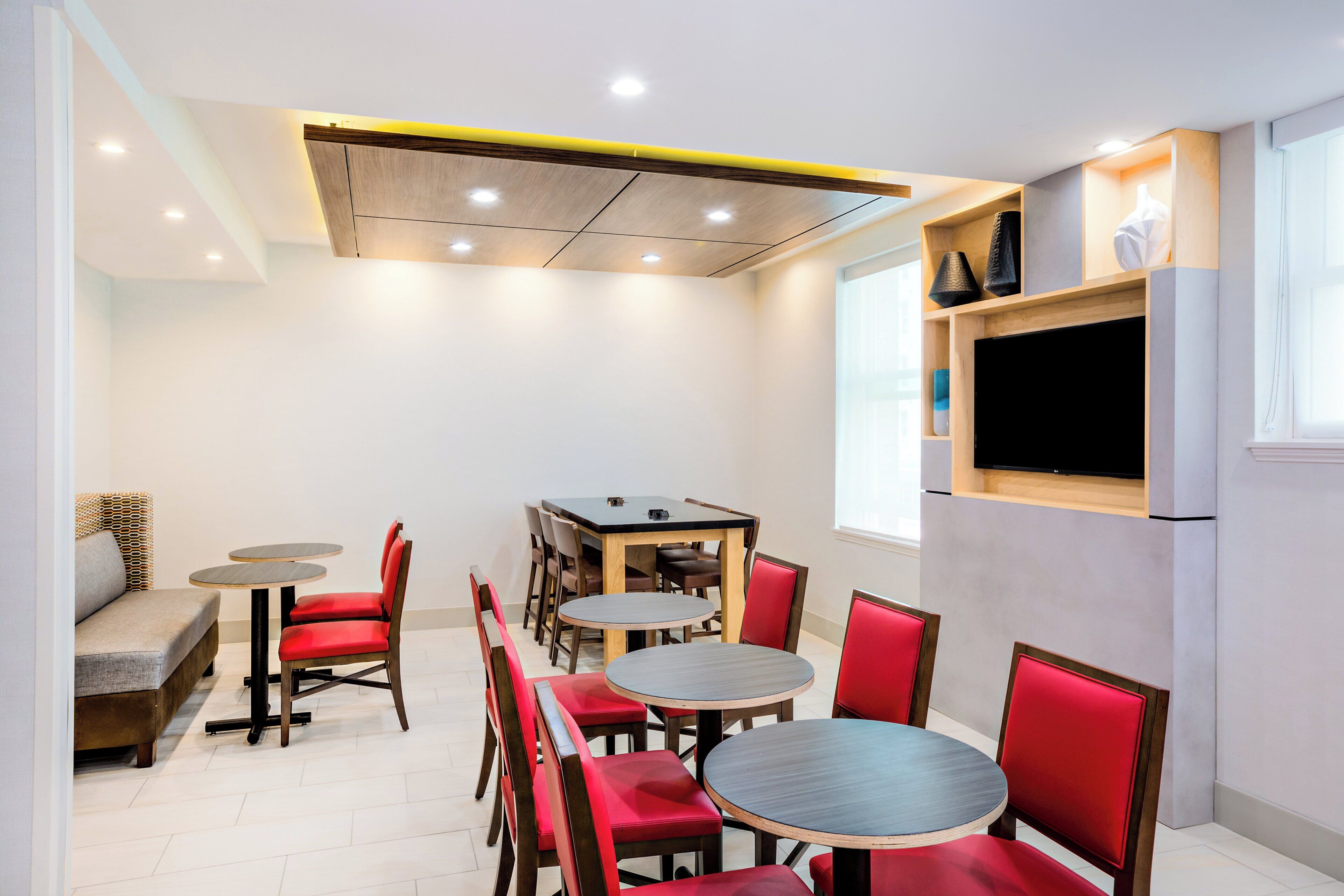 A modern dining area with a wooden ceiling, a built-in TV, and red upholstered chairs.