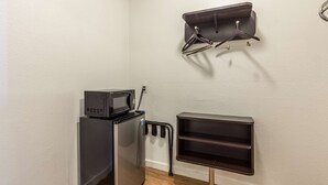 Una kitchenette compacta con microondas, un refrigerador pequeño y una repisa en la pared con perchero.