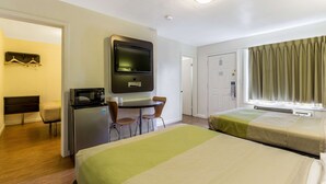 A hotel room with two beds, a desk with a TV, a microwave, and a chair.