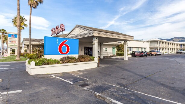 A motel with a prominent '6' sign, a covered entrance, and a parking lot with several cars.