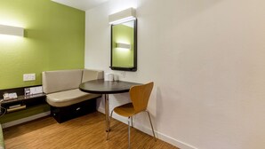Una habitación pequeña y moderna con una pared de acento verde, una mesa redonda con una silla, un espejo y un rincón de descanso con un sofá.