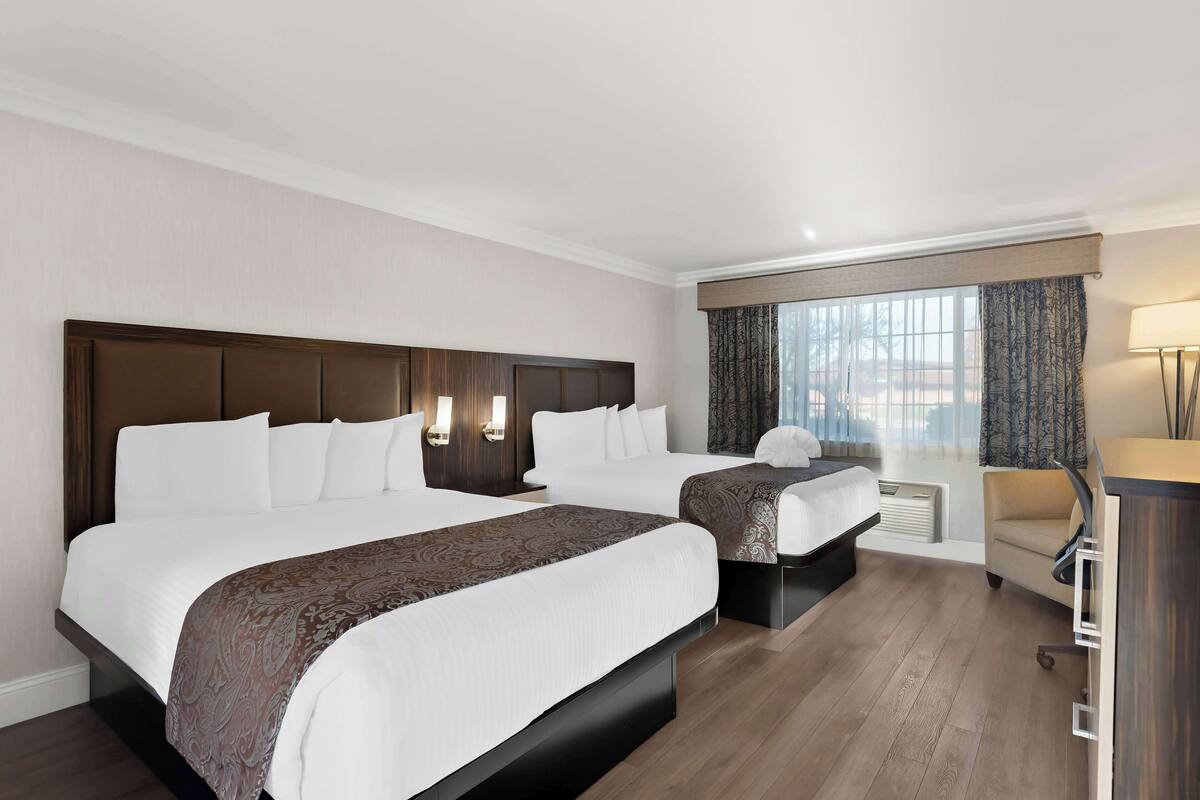 A hotel room with two beds, a desk, and a window with curtains.