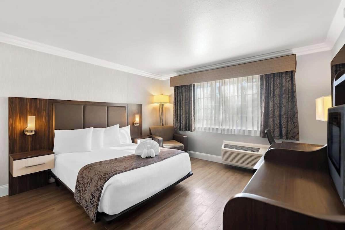 Ett hotellrum med en stor säng, sänglampor, ett skrivbord, en stol, en tv och ett fönster med gardiner.