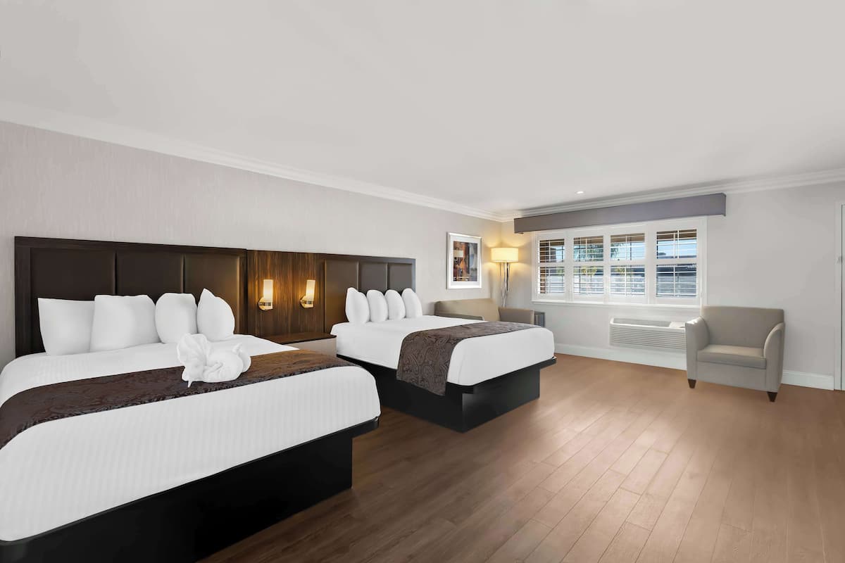 Ett hotellrum med två sängar, en soffa, ett fönster med persienner och en väggmonterad värmare.