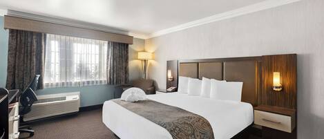 A hotel room with a large bed, a desk, a chair, a lamp, and a wall-mounted phone.